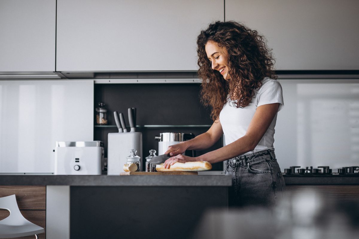 Uma mulher sorridente enquanto corta pão na mesa da cozinha ilustras nosso artigo sobre: Cinco mitos sobre atenção plena.