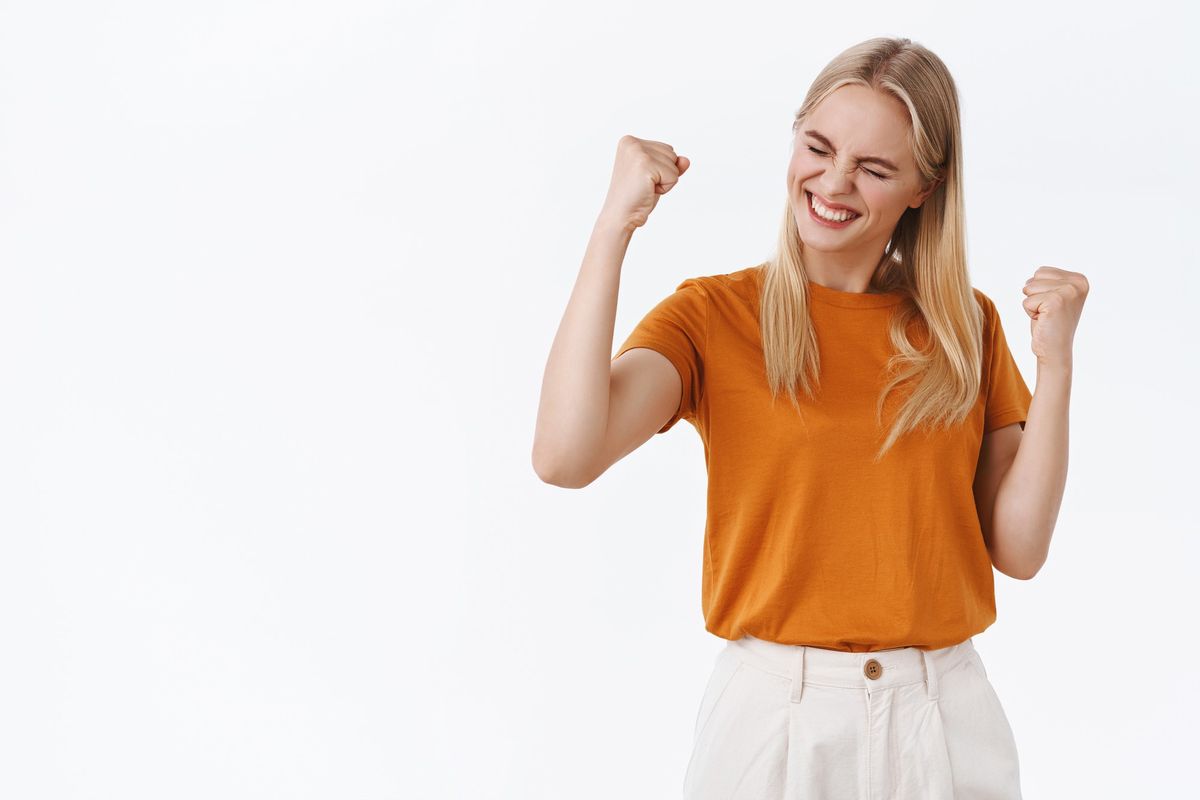 Uma mulher loira demonstrando felicidade ao obter uma vitória ilustra nosso artigo sobre: Por que celebrar pequenas conquistas?