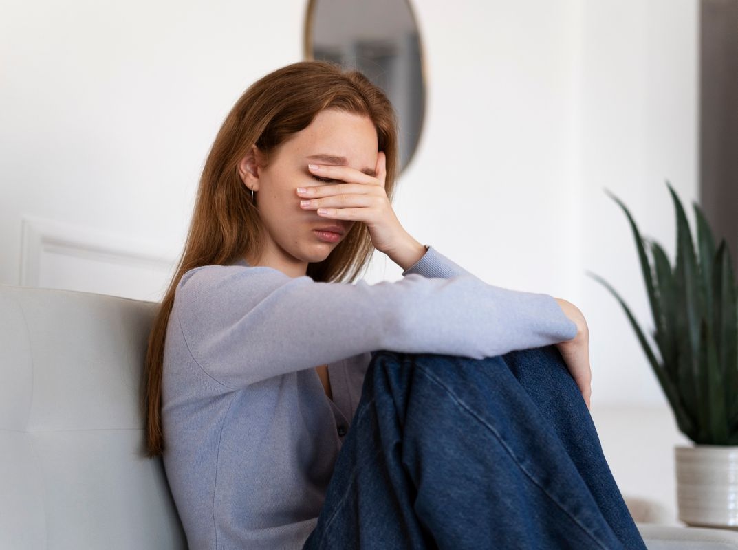 Uma mulher jovem sentada no sofá com a mão no rosto demonstrando decepção ilustra nosso artigo sobre: Sentir-se perdida: descubra o que é importante para você.