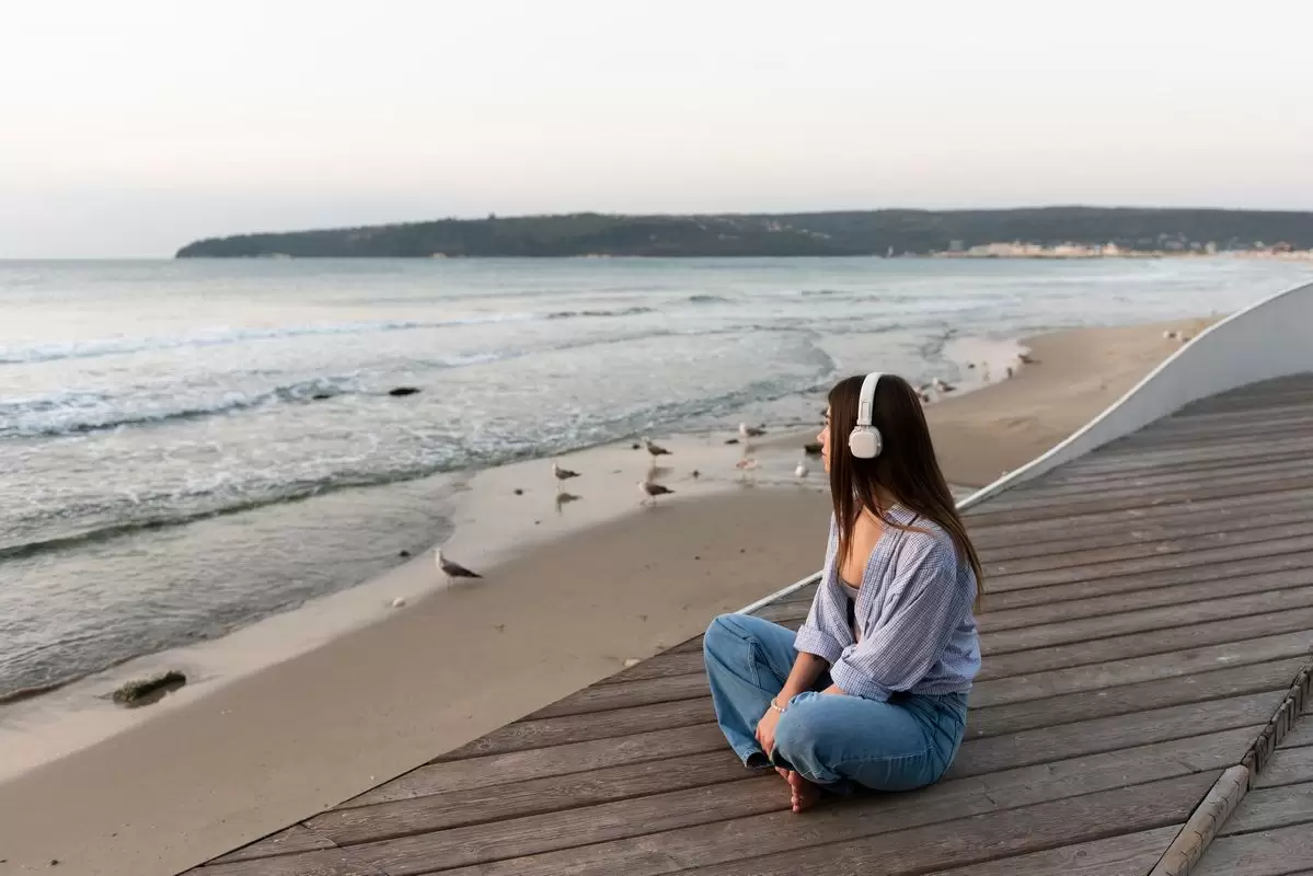 Uma mulher usando fones de ouvido observando o mar ilustra nosso artigo sobre solidão: transforme-a em sua aliada.