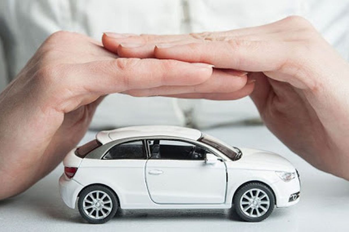 Uma pessoa fazendo uma casinha com as mãos demonstrando gesto de proteção sobre uma miniatura de automóvel. 