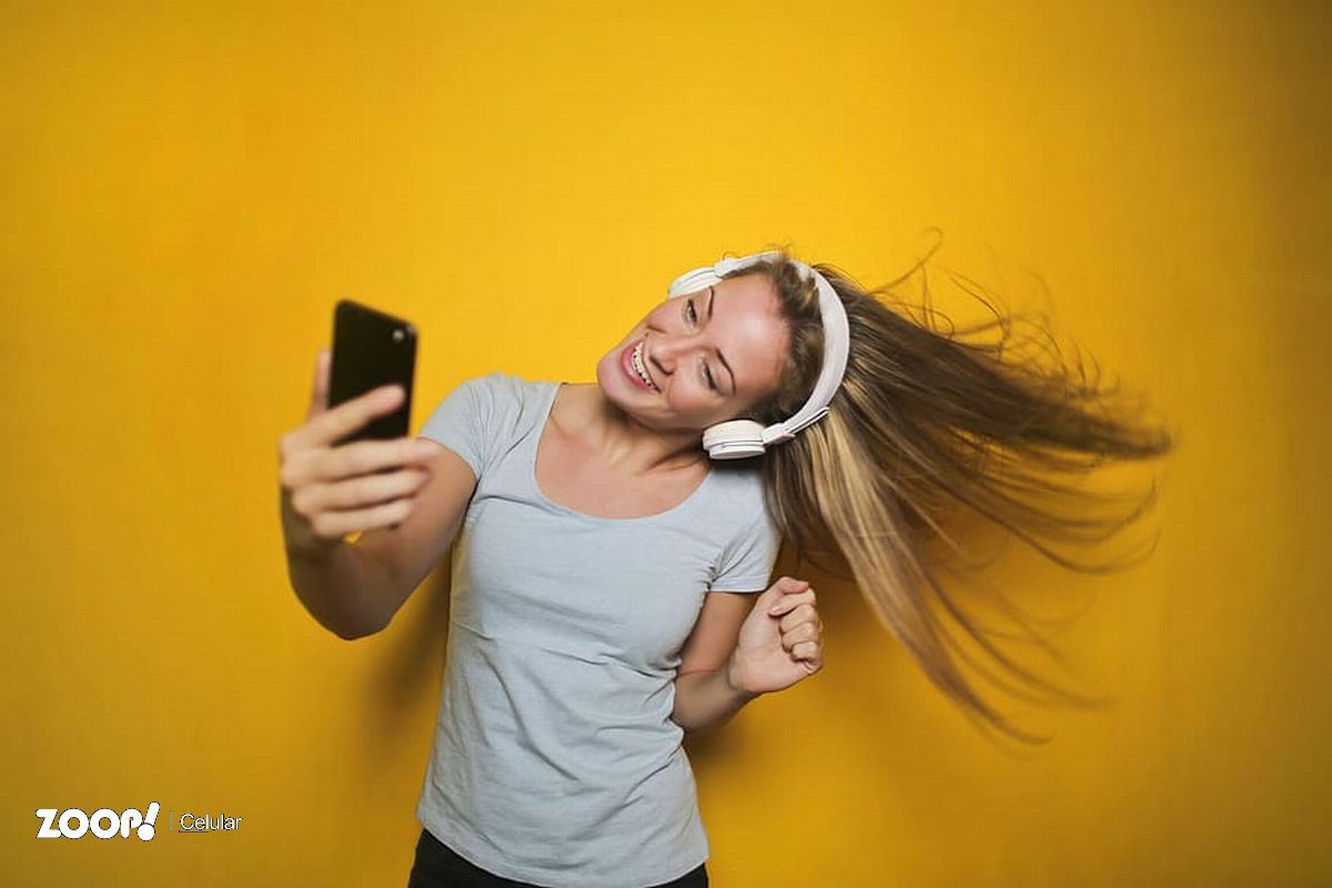  Jovem dançando e ouvindo música com fones de ouvido sem fio conectados ao telefone inteligente, ilustra nosso artigo sobre: Como colocar música de chamada no celular Vivo. (imagem: wallpaperflare)
