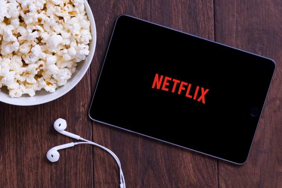 Um tablet mostrando a marca da Netflix ao lado de uma bacia de pipoca.