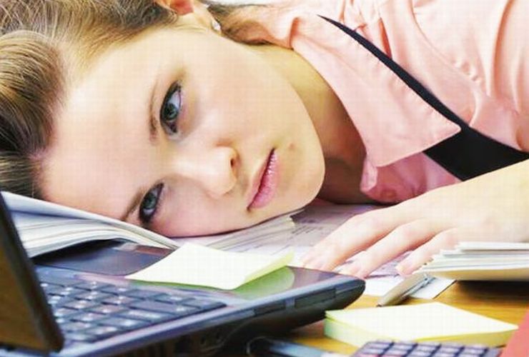 Uma mulher debruçada sobre o notebook demonstrando cansaço ilustra nosso artigo sobre: Como distribuir conteúdo nas redes sociais.
