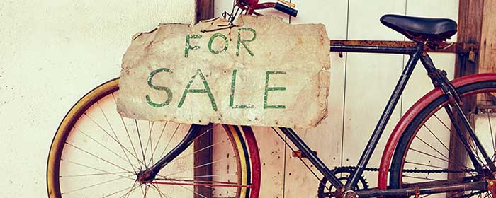 Uma bicilcleta antiga encontada numa porta, com uma placa de vende-se escrita em inglês.