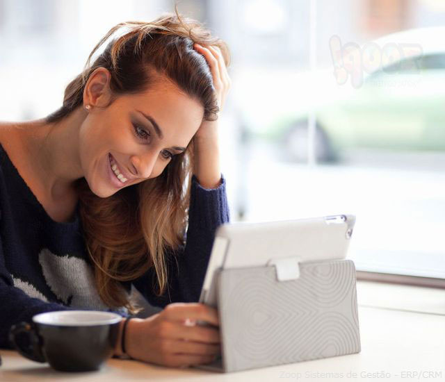 Um mulher jovem, sorrindo, usando um tablet numa chamada de vídeo.