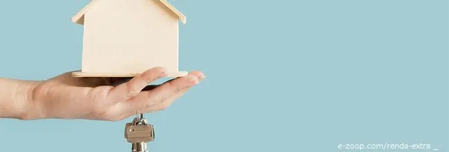 Uma mão segurando Uma pessoa segura uma casa em miniatura e um molho de chaves para demonstrar que se pode ganhar renda extra com aluguel.