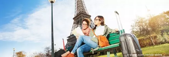 Duas mulheres jovens sentadas num banco de praça tendo ao fundo a torre Eifel.