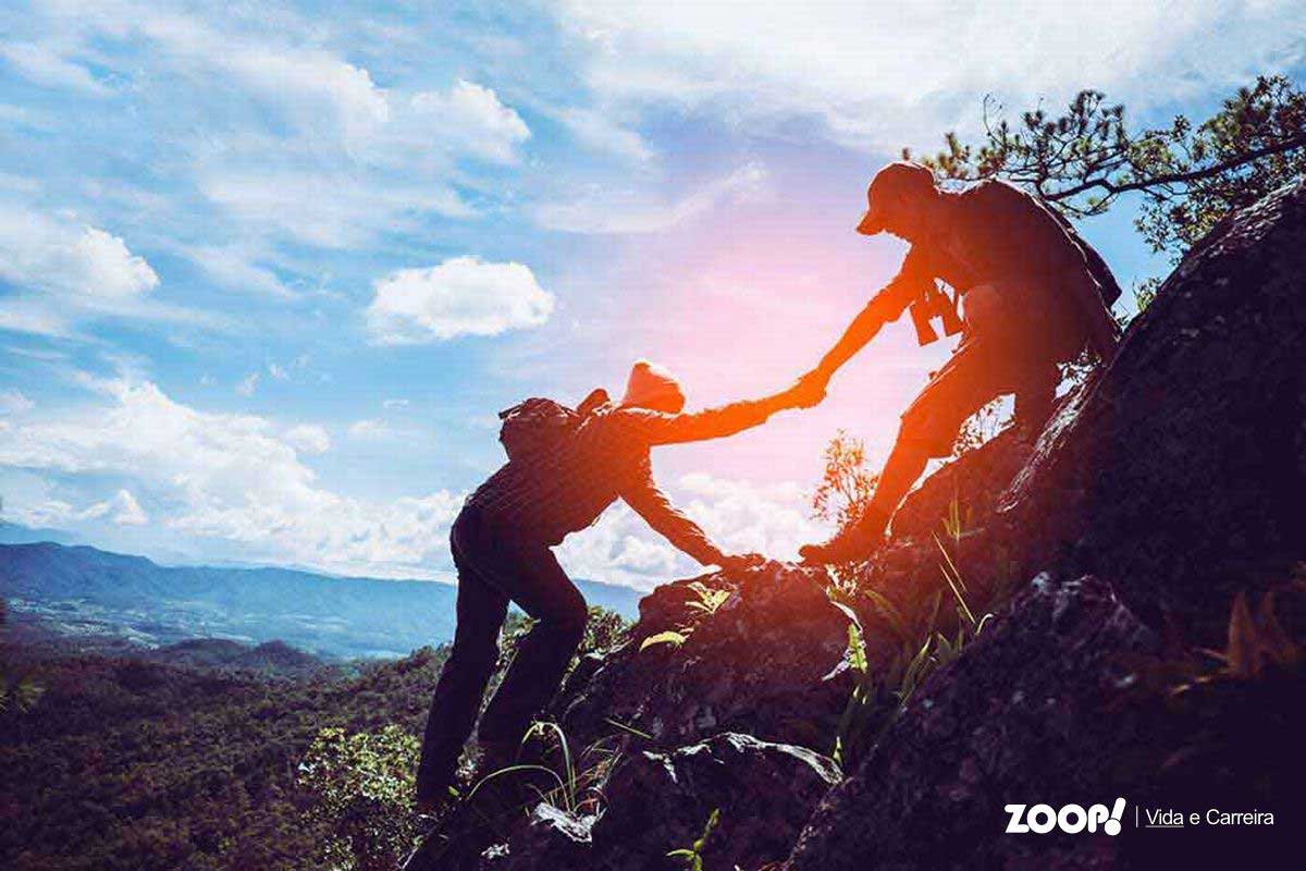 Uma pessoa ajudando outra durante uma escalada numa montanha, ilustra o nosso artigo sobre: Porque você deveria se tornar um mentor. 
