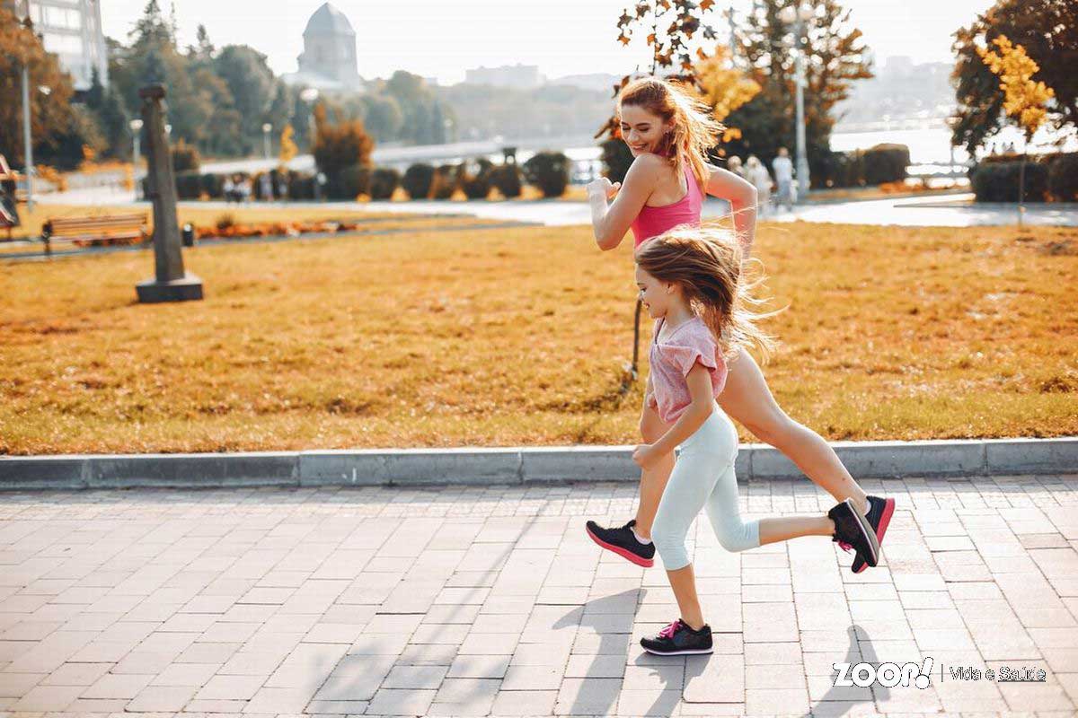 Mulher jovem e menina de 10 anos correm no parque num lindo dia de sol.