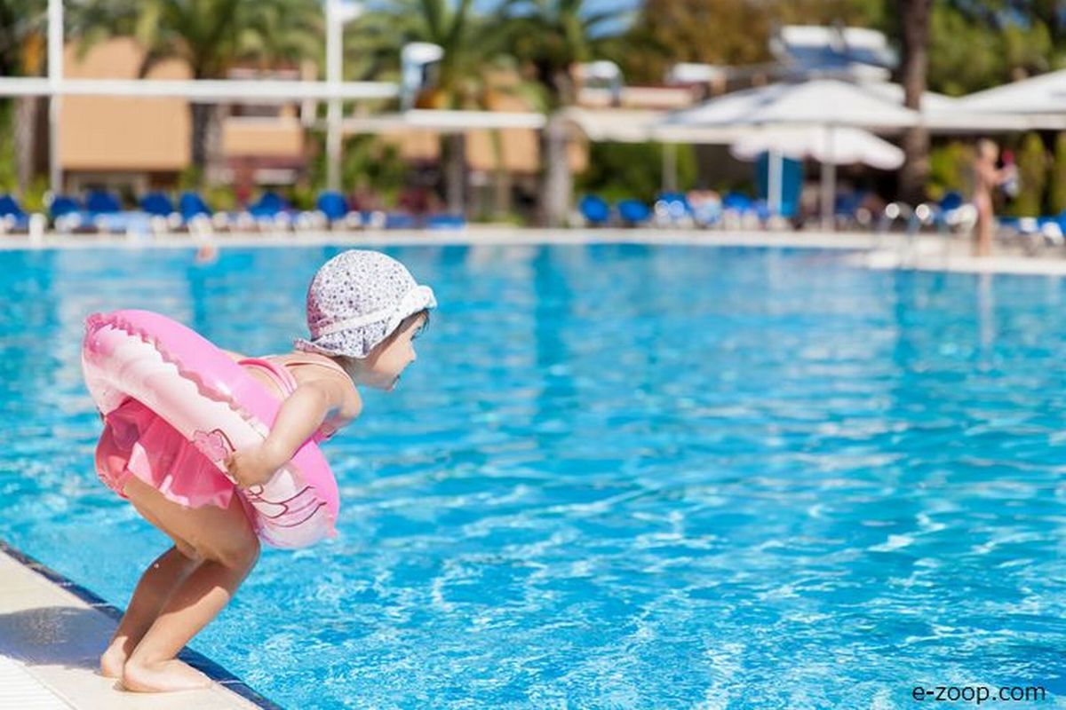 Uma criança de três anos pulando da beira de uma grande piscina ilustra nosso artigo sobre: Os 10 perigos da piscina que todos os pais precisam saber.