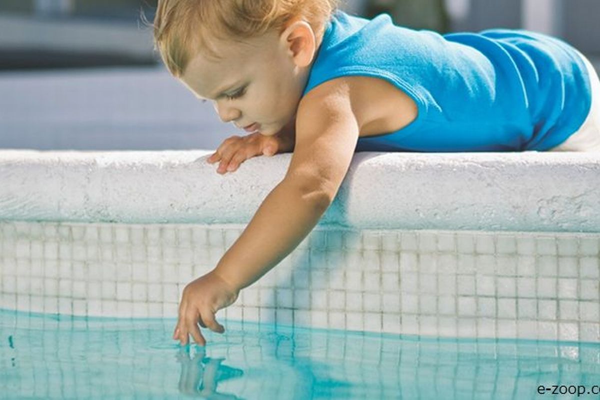 Uma criança de três anos brinca na beira de uma grande piscina ilustra nosso artigo sobre: Os 10 perigos da piscina que todos os pais precisam saber.