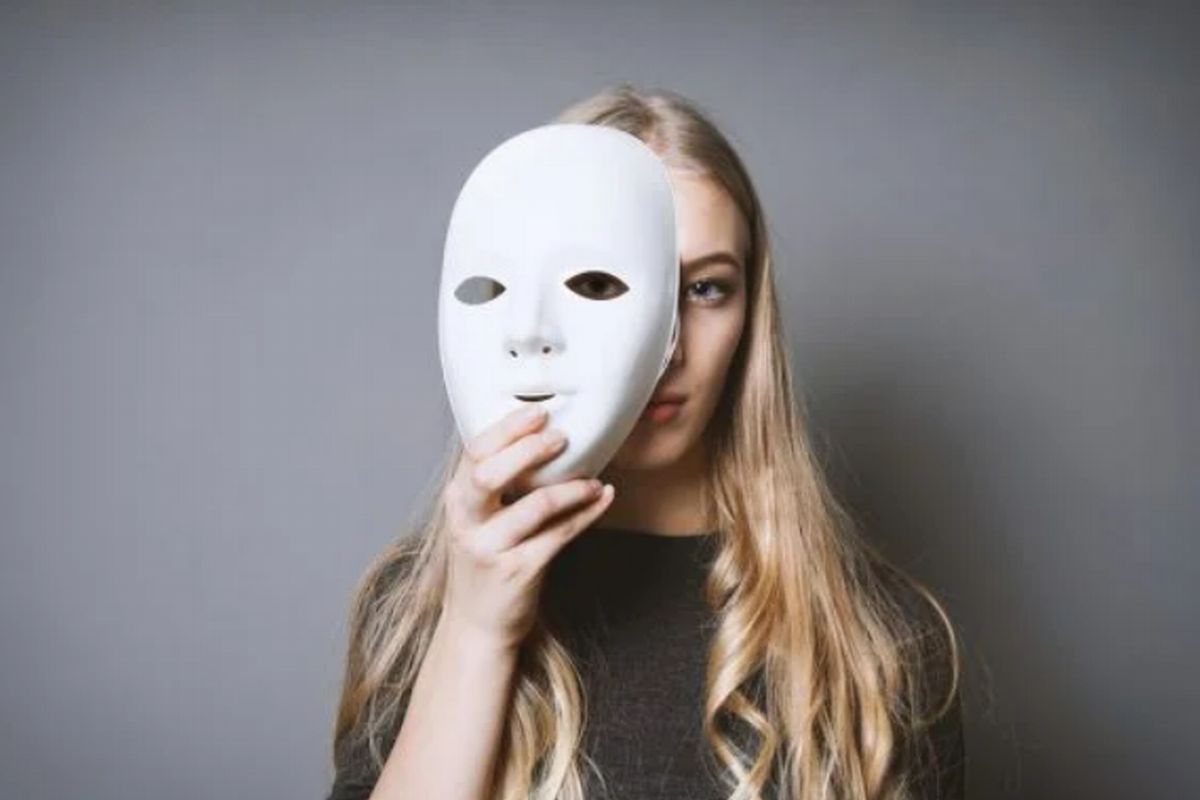 Uma mulher loira retirando a máscara ilustra nosso artigo sobre a síndrome do impostor.