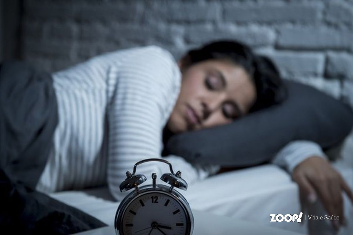 Uma mulher dormindo tendo um relógio despertador ao lado ilustra nosso artigo sobre: Como regular o sono e dormir melhor: confira algumas dicas.